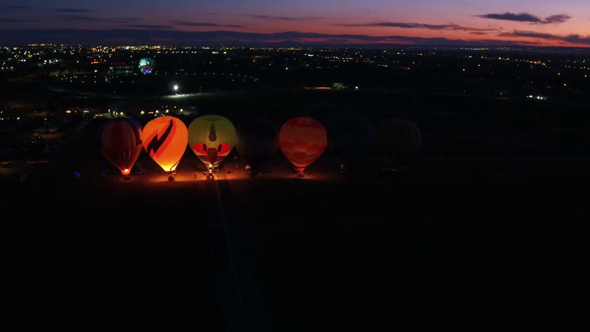 Balloon Fiesta Park from the air at dusk, balloons on the field and the lights of Albuquerque along the horizon